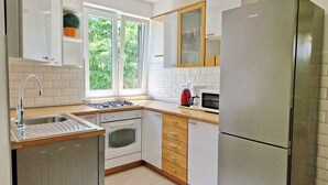 A modern kitchen with white cabinets, a stainless steel refrigerator, a built-in oven, and a window with a view of greenery. - Holiday flat with air conditioning and terrace (Baška)