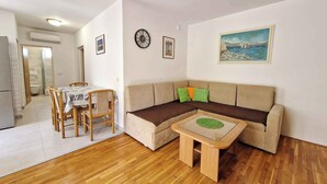 A compact living space with a sofa, a small table, a dining area with chairs, and a painting on the wall. - Holiday flat with air conditioning and terrace (Baška)