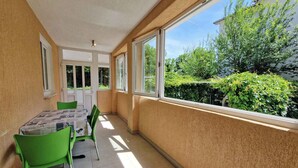 A balcony with a table and chairs, large windows, and a view of greenery. - Holiday flat with air conditioning and terrace (Baška)