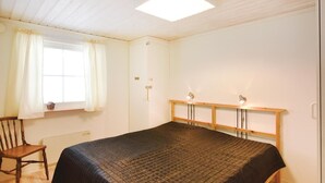 Een slaapkamer met een bed, een stoel, een raam met gordijnen en een plafondlamp.