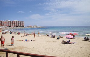 A beach with people sunbathing and swimming, umbrellas, and a building in the background. - 2 bedroom cozy apartment in Torrevieja (Torrevieja)