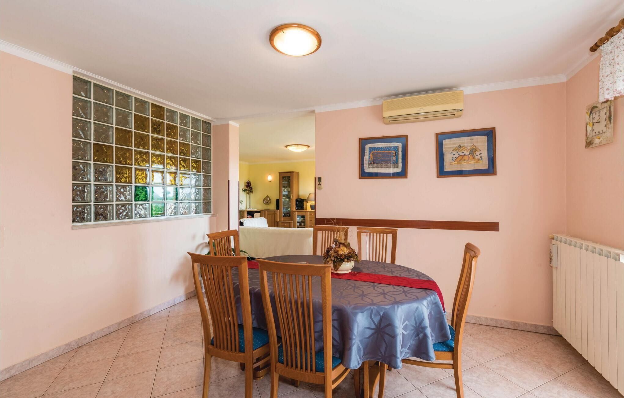A dining area with a round table, four wooden chairs, a blue tablecloth, and a window with decorative glass.