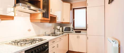 A kitchen with a gas stove, oven, microwave, and a window.