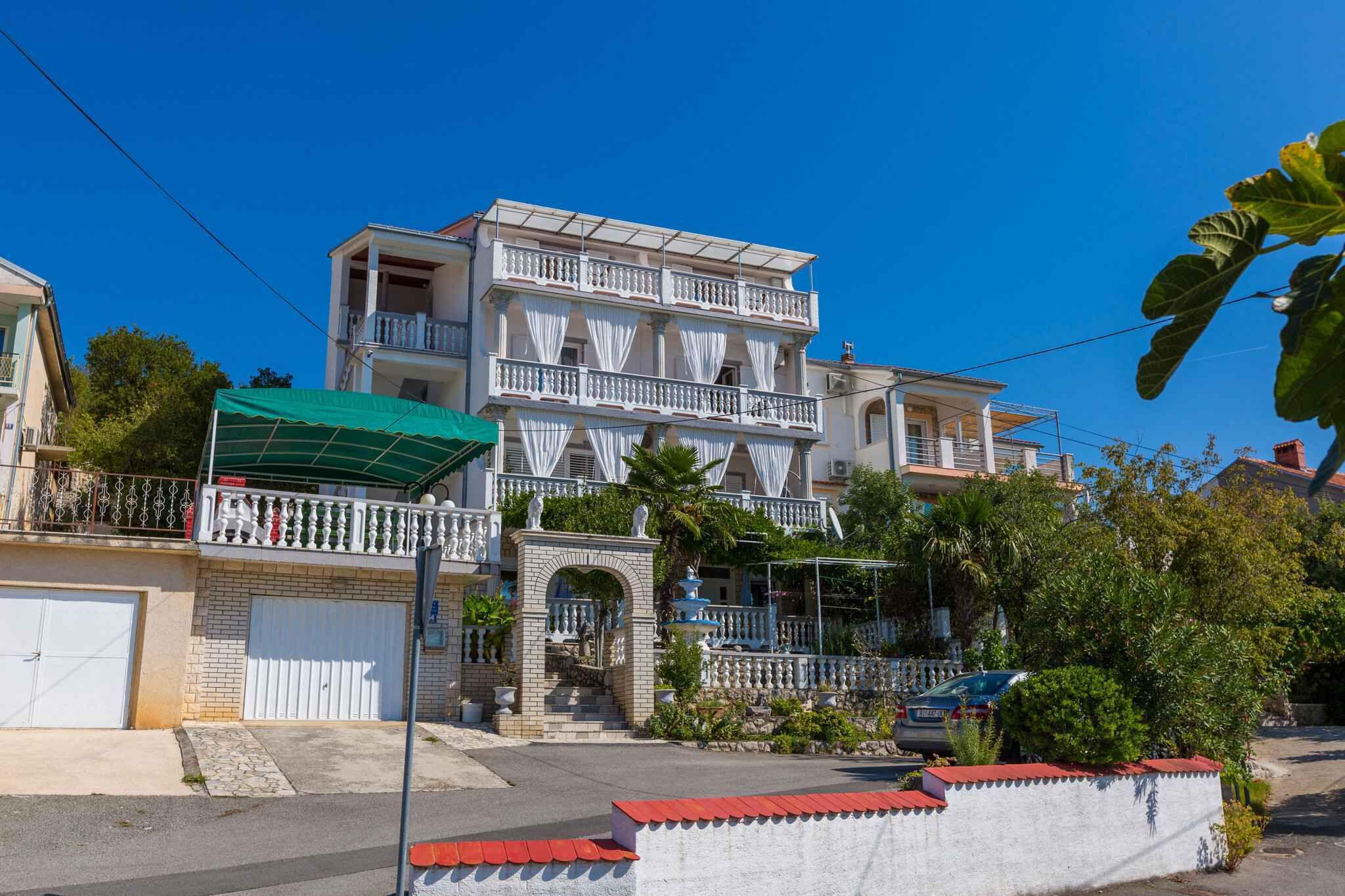 Um edifício residencial com vários andares, varandas, uma entrada com portão e uma pequena fonte.