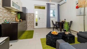 Une cuisine moderne avec des meubles de couleur sombre, une cuisinière encastrée et un pare-feu en pierre. On y trouve un coin repas avec une table et des chaises, ainsi qu’un salon avec un canapé et une table basse.