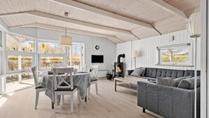 Un salón espacioso con chimenea, una mesa de comedor con sillas, un sofá y ventanas amplias que ofrecen vistas al exterior.