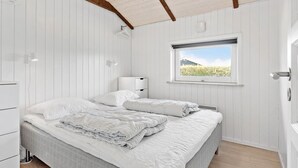 Un dormitorio con cama, mesitas de noche, ventana con vistas y techo con vigas a la vista.