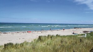 Una playa con arena, algunas personas y un primer plano con césped.