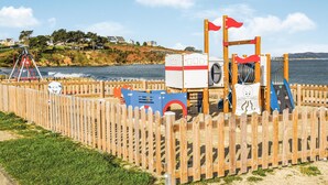 Un parque infantil en la playa con valla de madera, toboganes y un puesto de socorristas.