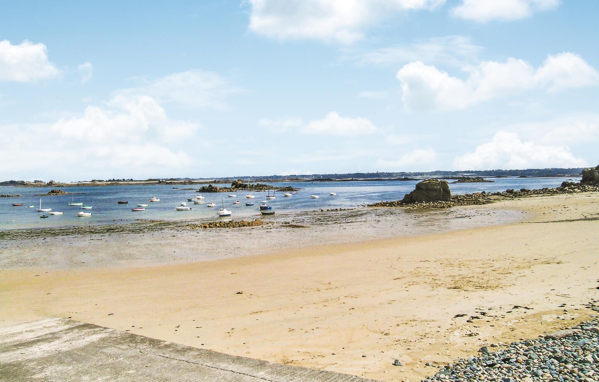 Une plage de sable parsemée de rochers, avec une eau calme.