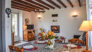 Un comedor con una mesa dispuesta para dos personas, un televisor y un jarrón decorativo con flores.