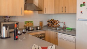 Una cocina con armarios de madera, microondas, hervidor, copas de vino, una botella de vino y una estantería para vinos.