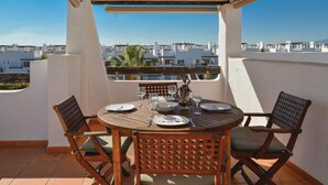 Una terraza con una mesa dispuesta para dos, con vistas a una zona residencial de edificios blancos y palmeras.