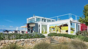 Un edificio moderno con fachada de vidrio, asientos al aire libre y un muro de piedra en primer plano.