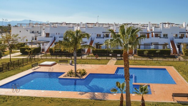 Un hotel moderno con piscina, palmeras y una vista despejada de las montañas al fondo.