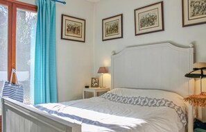 A bedroom with a white bed, a nightstand with a lamp, and framed pictures on the wall. - Amazing home in Tourrettes (Tourrettes)