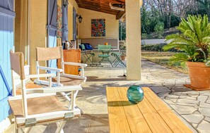 An outdoor seating area with a wooden table and a folding chair, a potted plant, and a colorful artwork on the wall. - Amazing home in Tourrettes (Tourrettes)