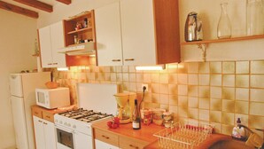 A compact kitchen with white cabinets, a gas stove, a microwave, and a sink. There is a shelf above the stove holding jars and a kettle. - 2 bedroom awesome home in Teyssieres (Teyssieres)