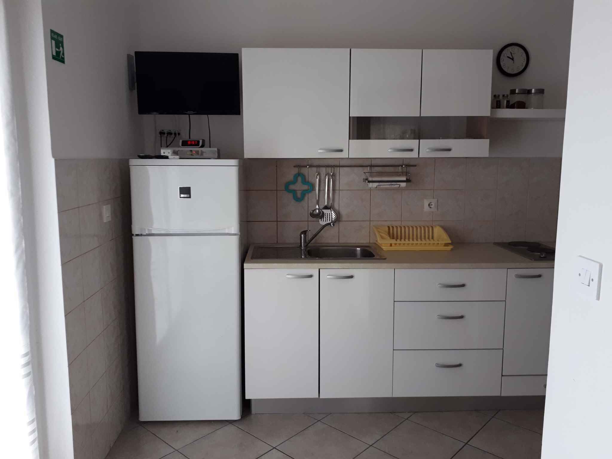 Cocina compacta con armarios blancos, refrigerador empotrado, pileta y un reloj en la pared.