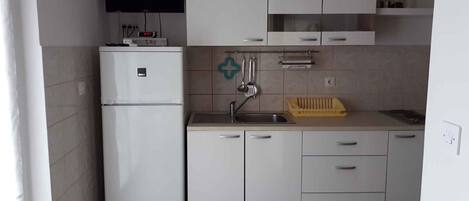 Cocina compacta con armarios blancos, refrigerador empotrado, pileta y un reloj en la pared.