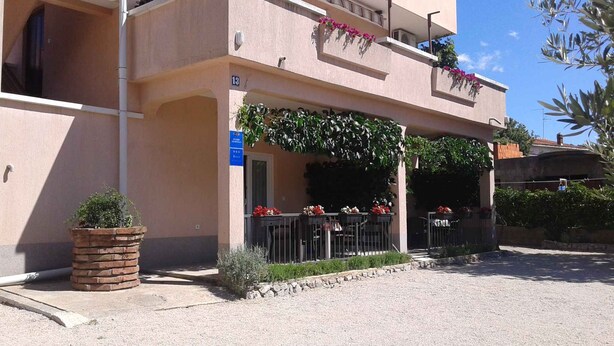 Un edificio de dos pisos con un espacio de asientos techado al aire libre, una jardinera de ladrillo y un letrero que indica un apartamento estudio.