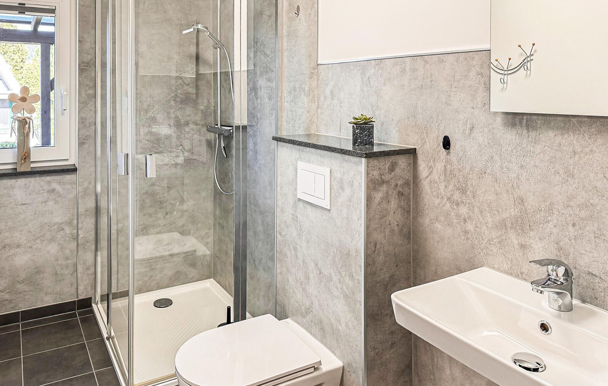 Een moderne badkamer met een douche met glazen wand, een wit toilet en een wastafel met spiegel.
