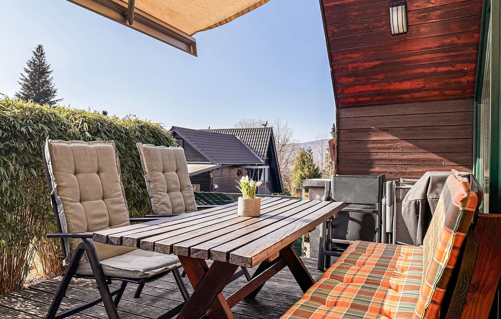 An outdoor patio with a wooden table, two cushioned chairs, a bench, and a small potted plant.