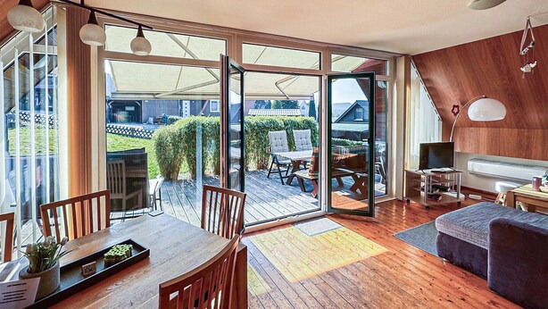A modern living room with a wooden floor, a dining area with a table and chairs, a sofa, a TV, and a sliding glass door leading to an outdoor patio. - Amazing home in Langelsheim with WiFi (Langelsheim)