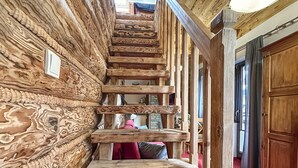 Un escalier en bois au design rustique, menant à une pièce dotée d’un mur en pierre et d’une porte en bois.