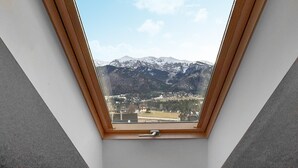 Une lucarne offrant une vue sur des montagnes enneigées et un petit village en contrebas.
