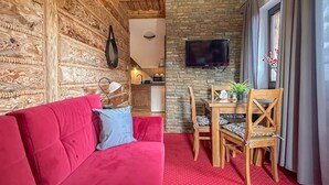 Une pièce chaleureuse avec un canapé rouge, une table à manger en bois et des chaises. On peut voir un mur en pierre et un plafond en bois.