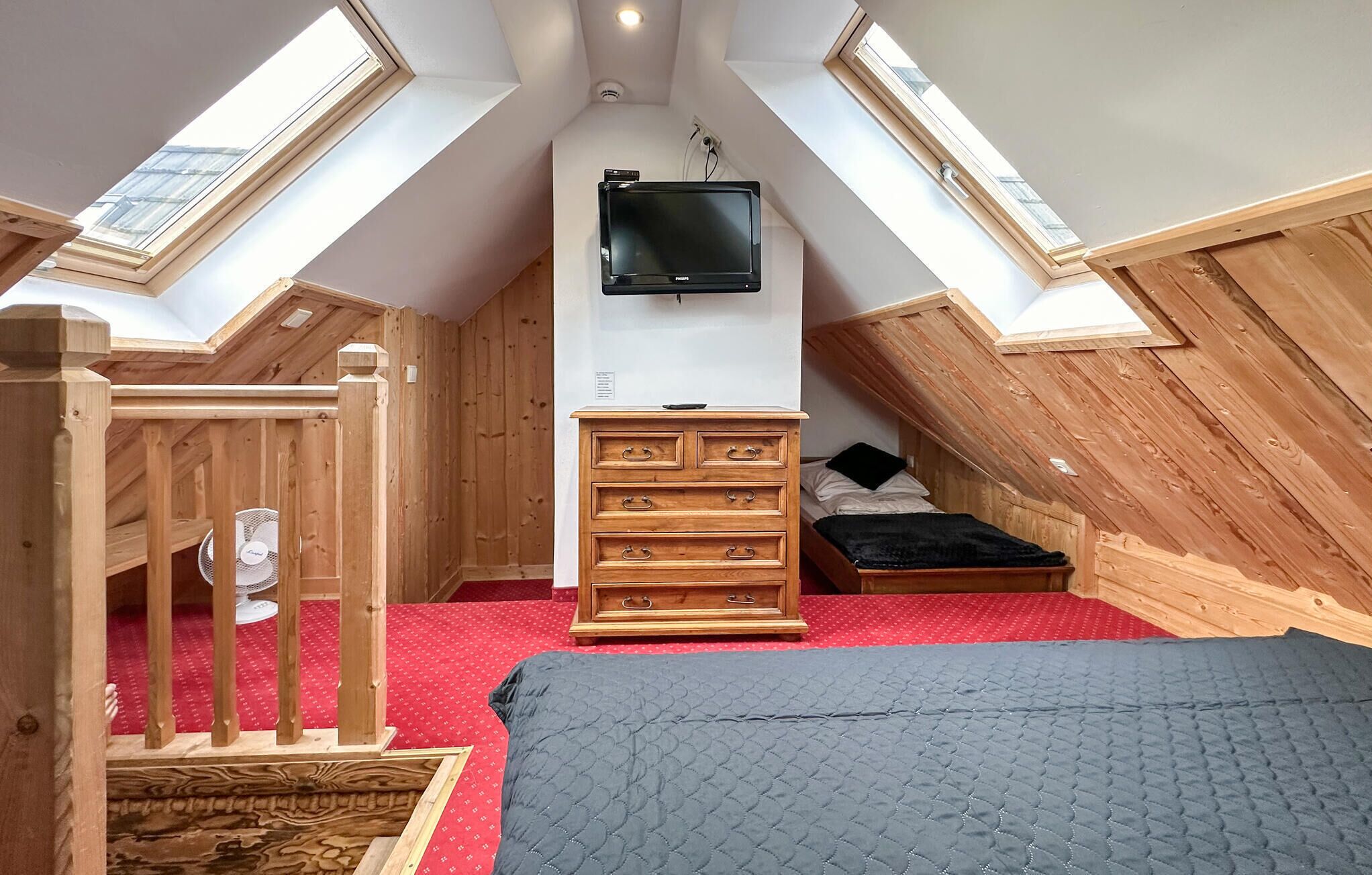Una camera in stile dormitorio con un letto a soppalco, un televisore fissato alla parete e una cassettiera in legno.