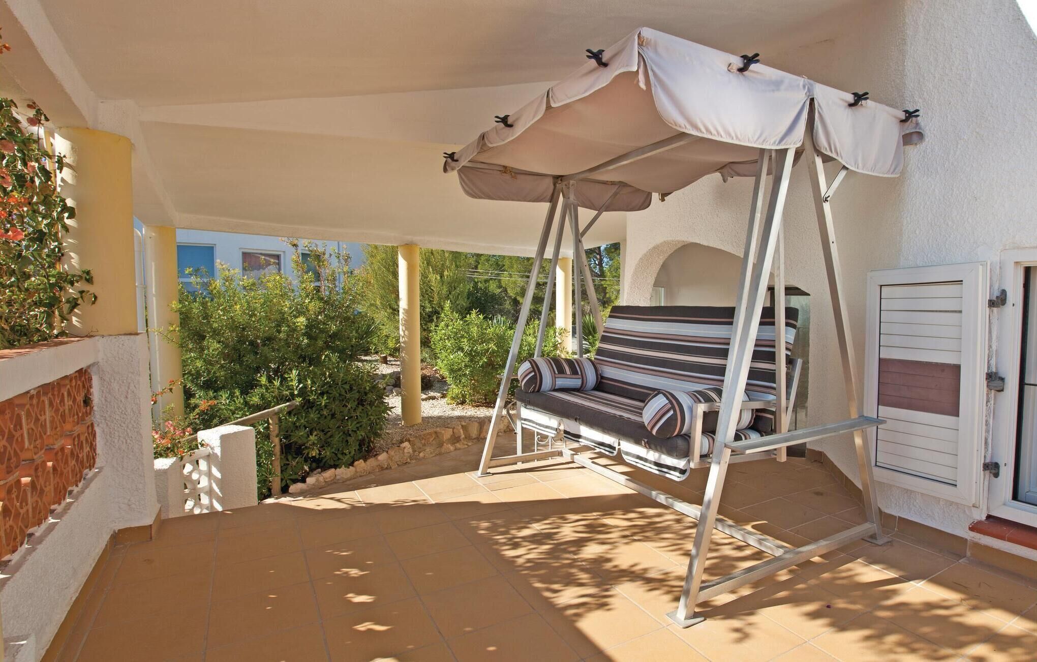 A covered outdoor seating area with a swing chair and a cushioned bench.