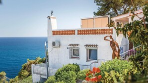 Un edificio costero con fachada blanca, una ventana pequeña con rejilla metálica y una escultura de figura humana.
