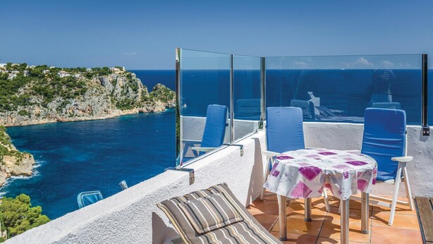 Una terraza con vistas despejadas al mar, una mesa con mantel y sillas azules.