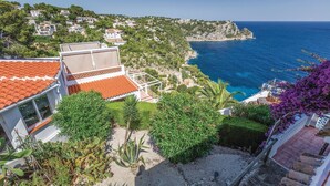 Zona residencial costera con casas escalonadas, vista despejada del mar y un jardín con diversas plantas.