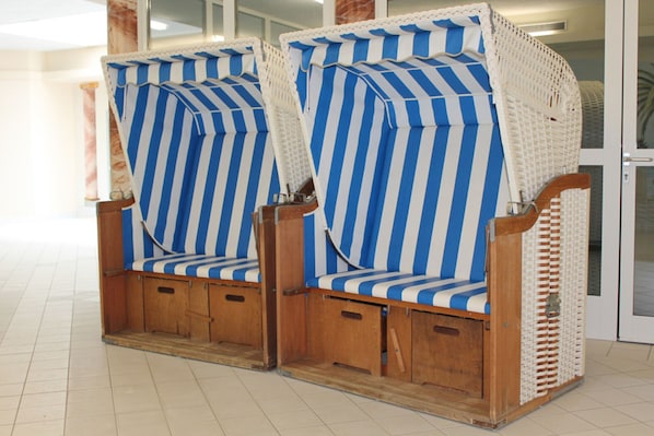 Deux chaises de plage à rayures, dotées d’une structure en bois et de compartiments de rangement, placées dans un espace intérieur carrelé.