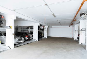 Un parking souterrain où plusieurs voitures sont garées dans des emplacements prévus à cet effet, avec un sol en béton et des tuyaux apparents au plafond.