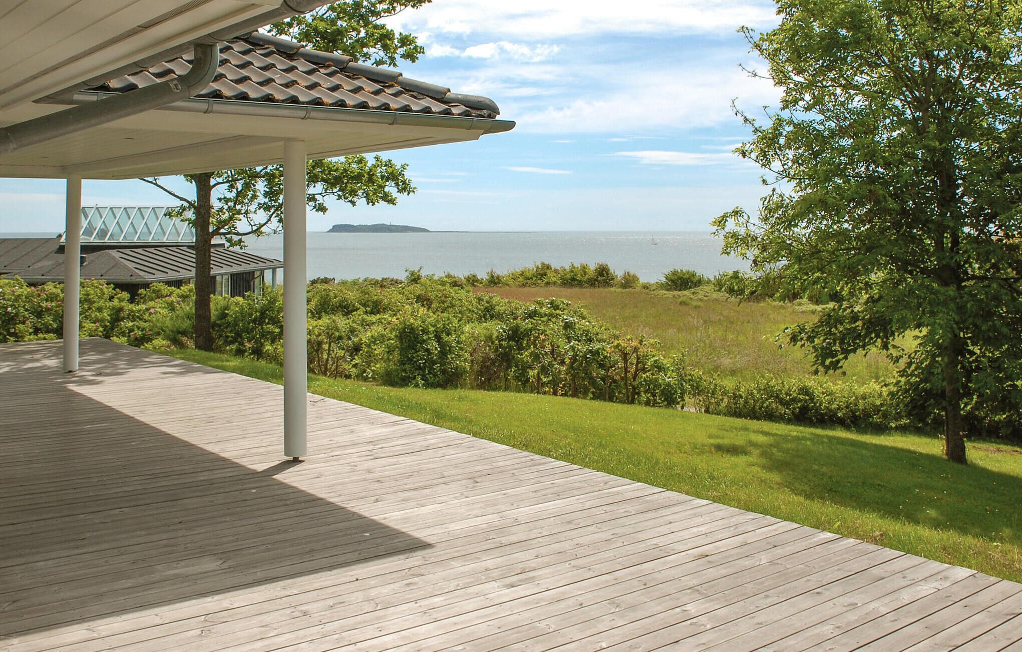 Ett trädäck med en pergola, med utsikt över en gräsyta med träd och havet.