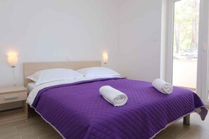 Een bed met een paarse quilt, twee witte kussens en twee opgerolde handdoeken.