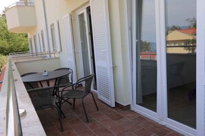 Een balkon met een tafel, stoelen, een schuifdeur en uitzicht op de omgeving.