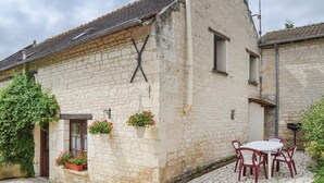 A stone building with a tiled roof, a door, and a window. There are potted plants on the wall and a table with chairs outside. - Awesome home in Assay (Assay)