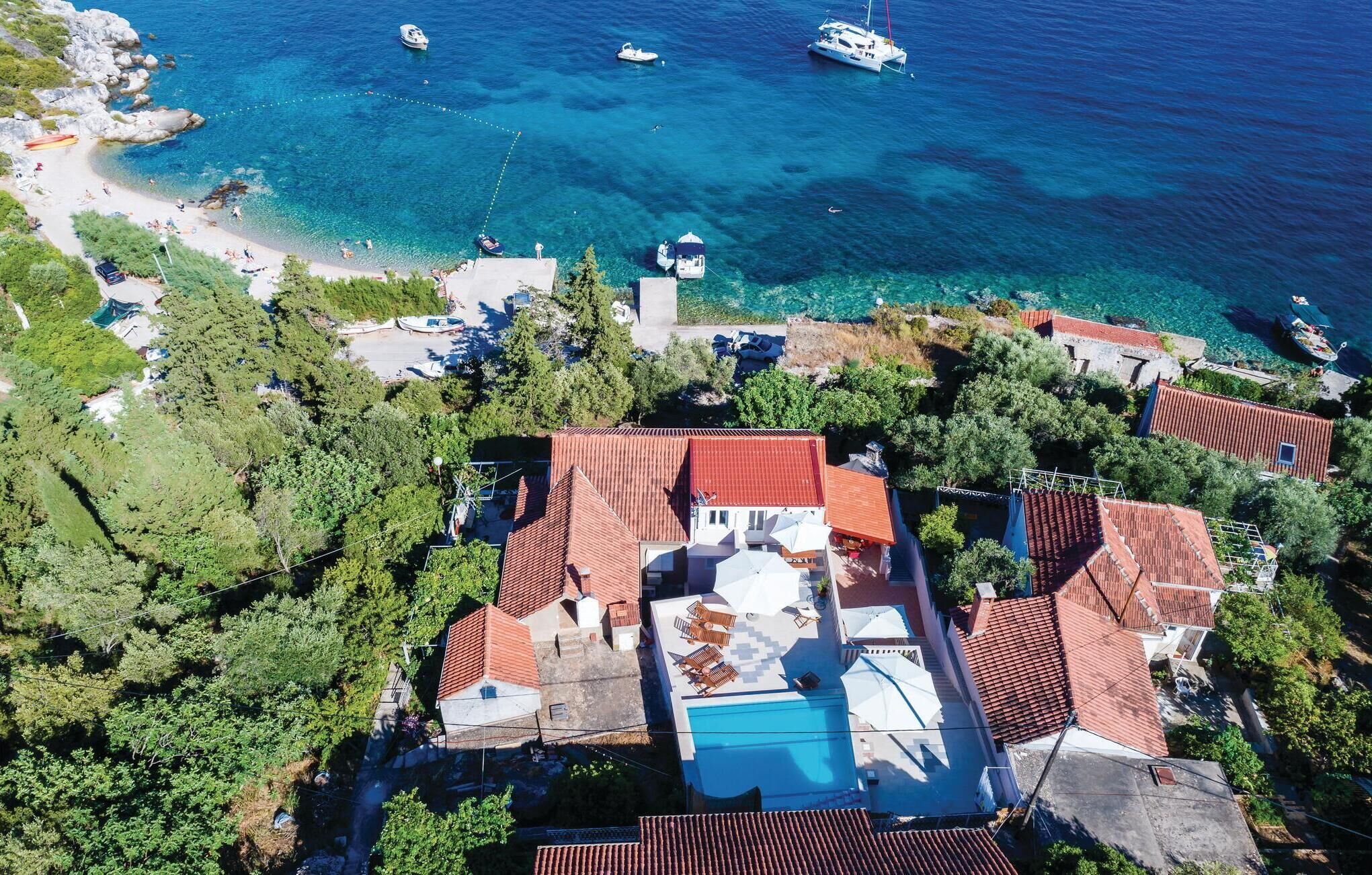 Vista aérea de uma propriedade costeira com piscina, casas em terraços e barcos na água.