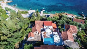 Luftaufnahme einer Küstenimmobilie mit Schwimmbad, terrassenförmig angelegten Häusern und Booten im Wasser.