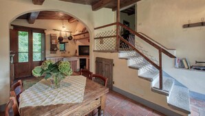 A rustic dining area with a wooden table, chairs, and a vase of flowers. A staircase with a wooden railing leads to an upper level. - 3 bedroom amazing home in Anghiari -AR- (Anghiari -AR-)