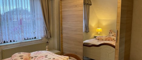 A bedroom with a bed, a dresser, a mirror, a radiator, and a window with curtains.