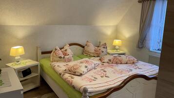 Una cama bien hecha con ropa de cama estampada, dos mesitas de noche con lámparas, un radiador y una ventana con cortinas.