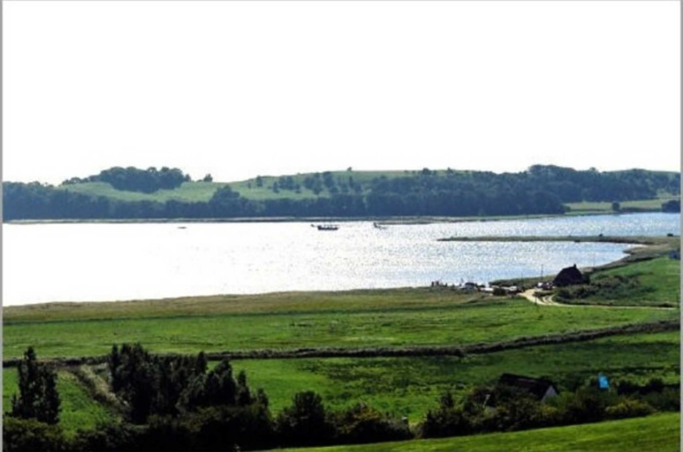 A coastal landscape with a body of water, grassy fields, and a distant hill.