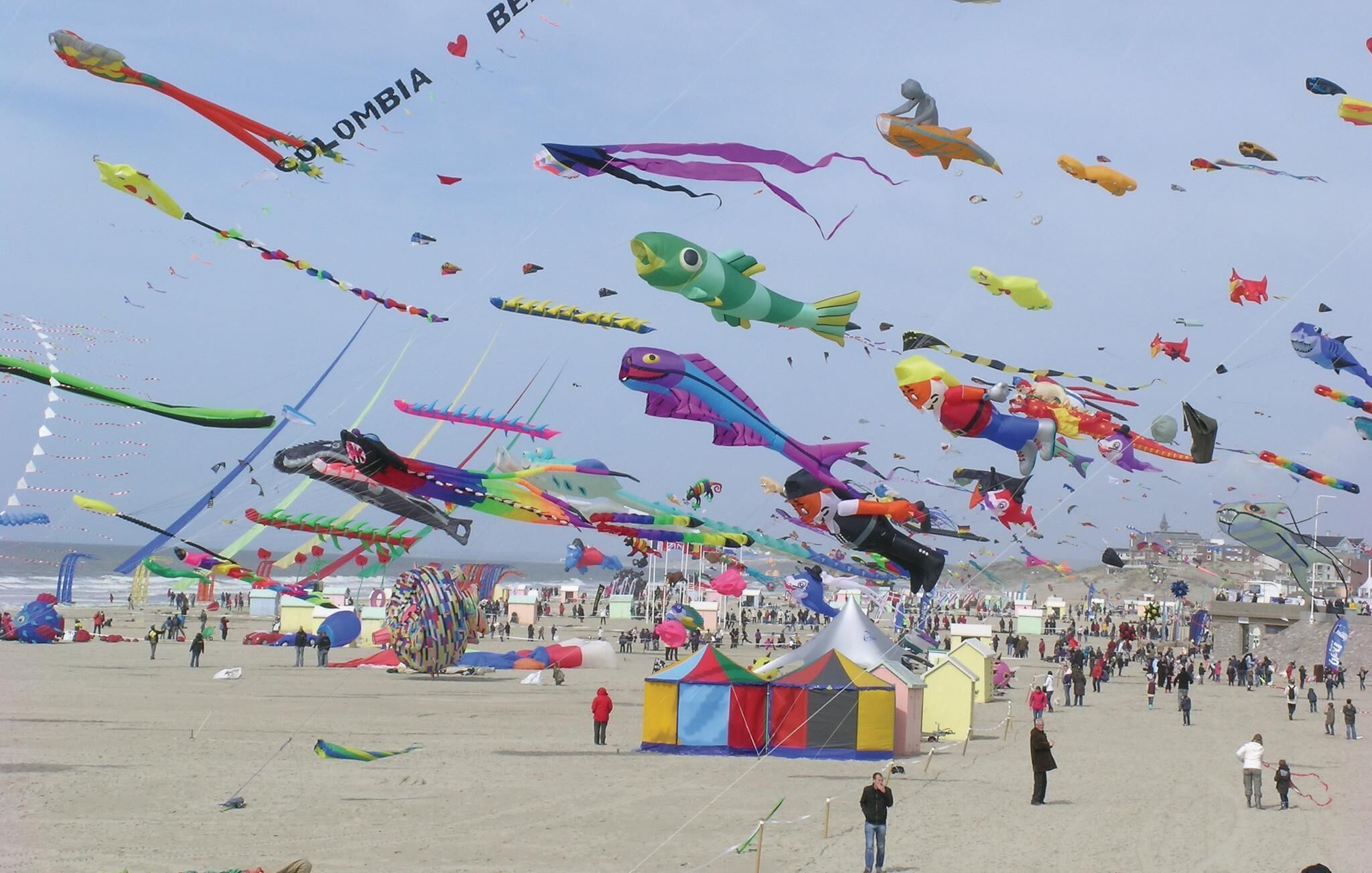 A beach with numerous colorful kites and tents.
