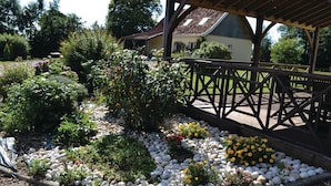 Um jardim com um deck de madeira, cercado por diversas plantas e flores.